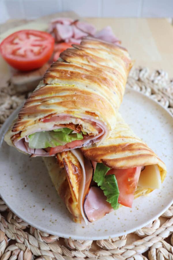 Cottage cheese flatbread wrap filled with ham, tomato and lettuce on a white plate.