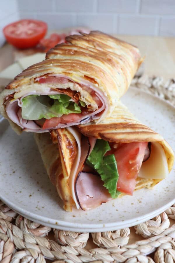 Cottage cheese flatbread wrap filled with ham, tomato and lettuce on a white plate.