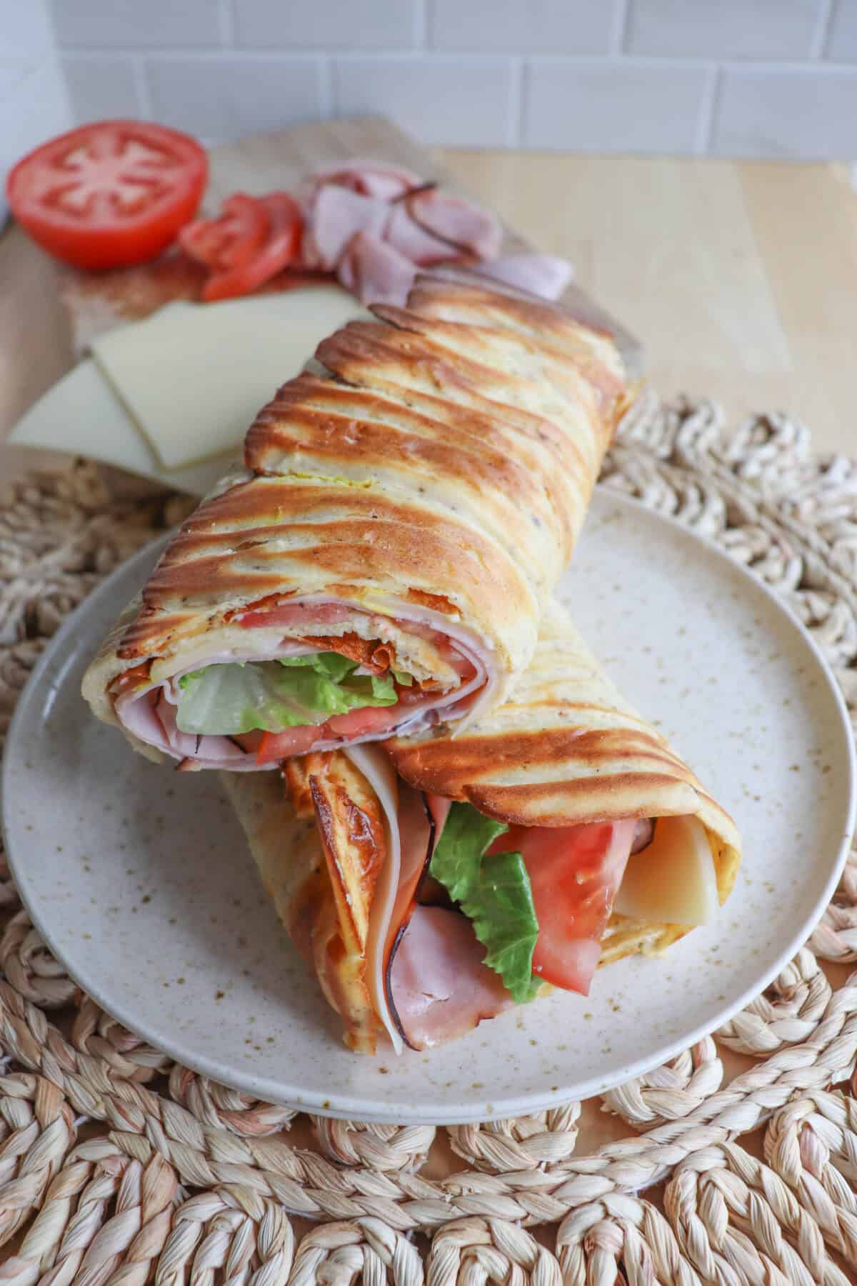 Cottage cheese flatbread wrap filled with ham, tomato and lettuce on a white plate.