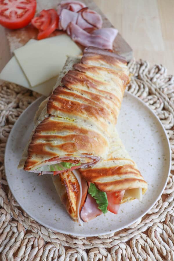 Cottage cheese flatbread wrap filled with ham, tomato and lettuce on a white plate.