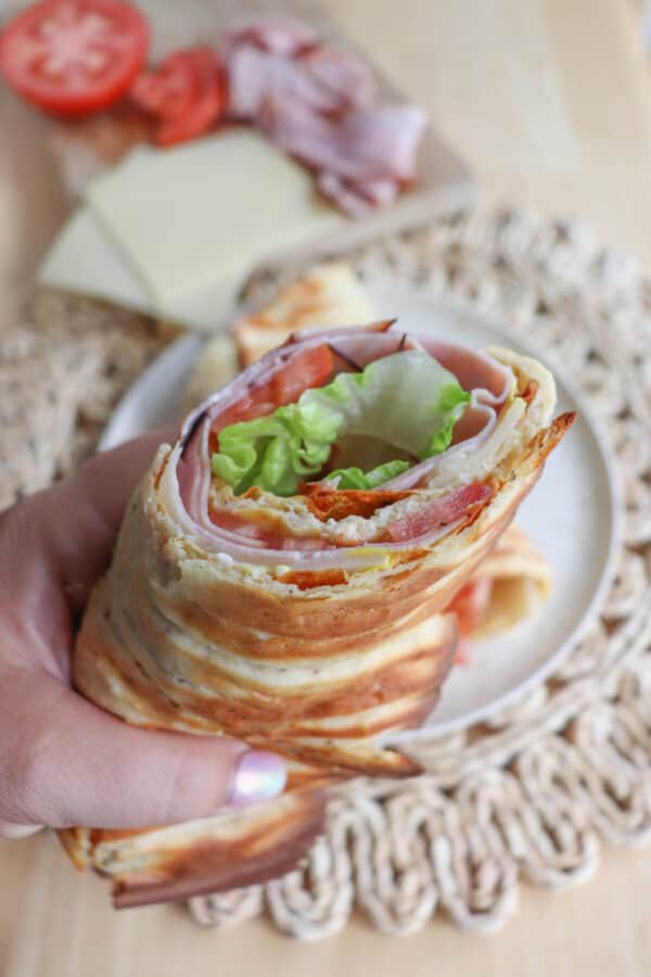 Cottage cheese flatbread wrap filled with ham, tomato and lettuce held in a hand.