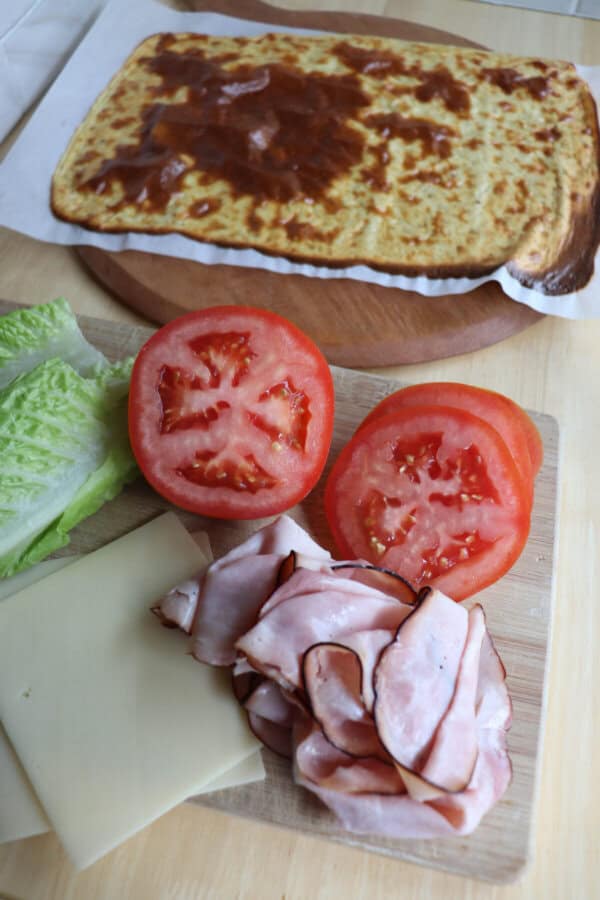 Cottage cheese flatbread with ham, sliced tomato and lettuce on a wooden table.