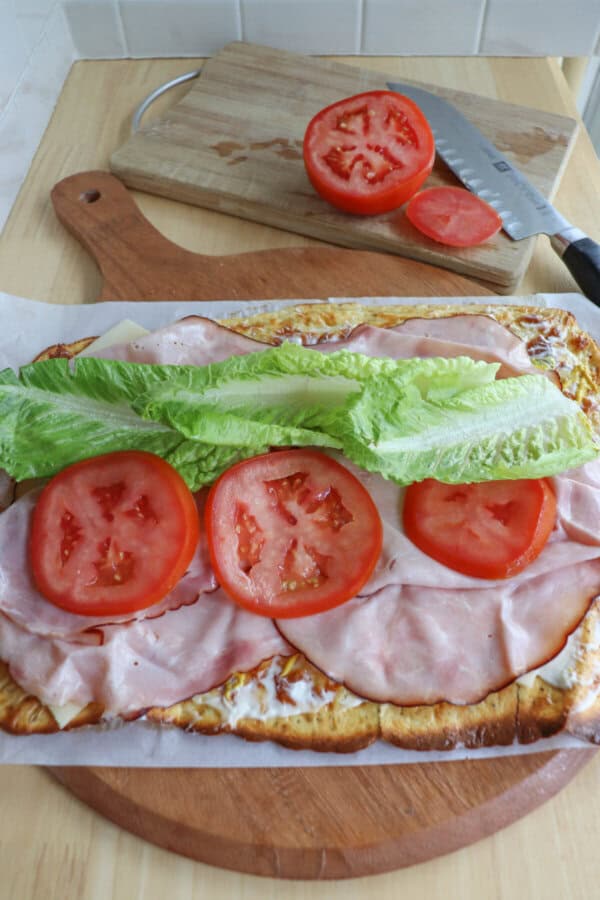 Cottage cheese flatbread with lettuce, sliced tomato and ham laid out on top.
