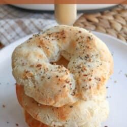 A stack of gluten-free air fryer bagels topped with seeds is displayed on a white plate. The background includes a woven placemat, and text at the top reads gluten free air fryer bagels. A website URL is at the bottom.