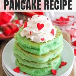 A stack of green pancakes on white plates topped with whipped cream and red heart candies.