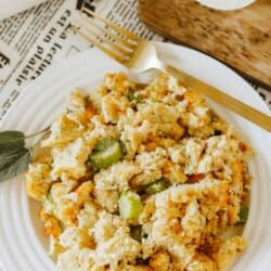 Cornbread stuffing with bread cubes, diced celery and onion bits on a white plate with a gold fork.