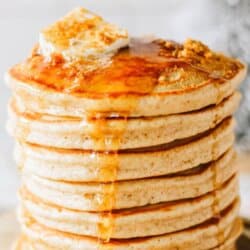 Fluffy gingerbread pancakes stacked on top of each other with a pat of butter on top and syrup dripping over the edges.