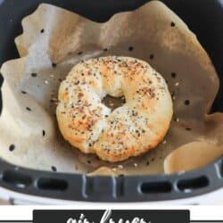 A homemade bagel with sesame and poppy seeds is baking inside an air fryer lined with parchment paper. The text below reads air fryer bagel recipe homemadeheather.com.