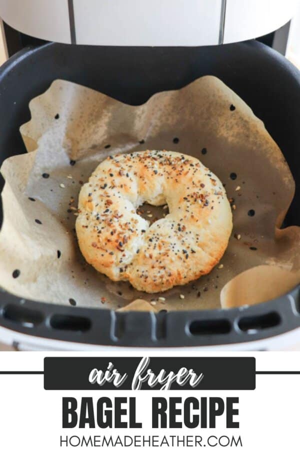 A homemade bagel with sesame and poppy seeds is baking inside an air fryer lined with parchment paper. The text below reads air fryer bagel recipe homemadeheather.com.