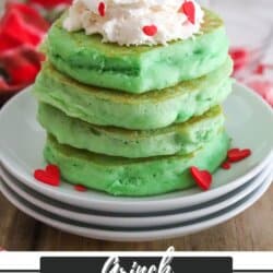 A stack of green pancakes on white plates topped with whipped cream and red heart candies.