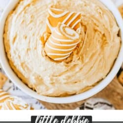 Creamy pumpkin spice dip in a white bowl topped with Little Debbie pumpkin rolls on a newspaper lined table.
