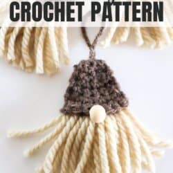 Crochet gnome ornament with cream beard and brown hat on a white surface.