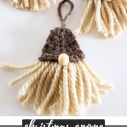 Crochet gnome ornament with cream beard and brown hat on a white surface.