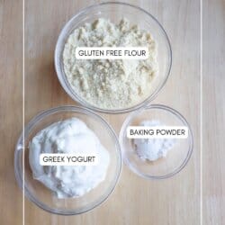 Three glass bowls on a wooden surface. The bowls contain labeled ingredients: Gluten Free Flour, Greek Yogurt, and Baking Powder. The website homemadeheather.com is visible at the bottom.