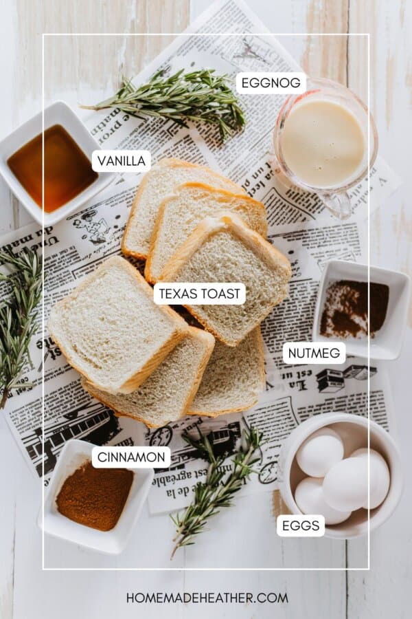 Top view of ingredients for French toast on a wooden surface, including slices of Texas toast, a glass of eggnog, bowls of vanilla extract, nutmeg, cinnamon, and whole eggs. Sprigs of rosemary and a newspaper complete the setup.