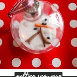Clear glass ball ornament with salt and snowman parts in it on a red background.