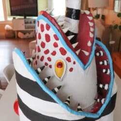 A sculpted mask designed to look like a sandworm with a large open mouth, sharp pointed teeth, red and white polka dots, and a striped black and white tongue sticking out.