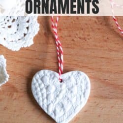 Heart shaped pressed clay ornament in white with red bakers twine on a wooden board.