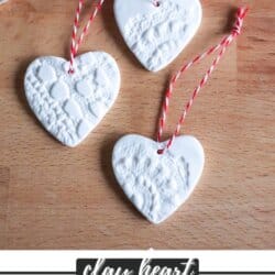Heart shaped pressed clay ornaments in white with red bakers twine on a wooden board.
