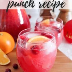 Pink Christmas Punch in a clear glass with fresh cranberries and orange wedges.