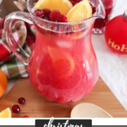 Pink Christmas Punch in a clear glass with fresh cranberries and orange wedges.