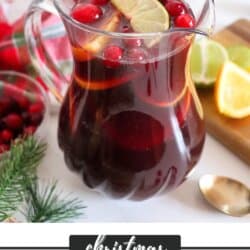 Red wine sangria in a clear glass pitcher with cranberries, lime slices and orange slices for garnish.