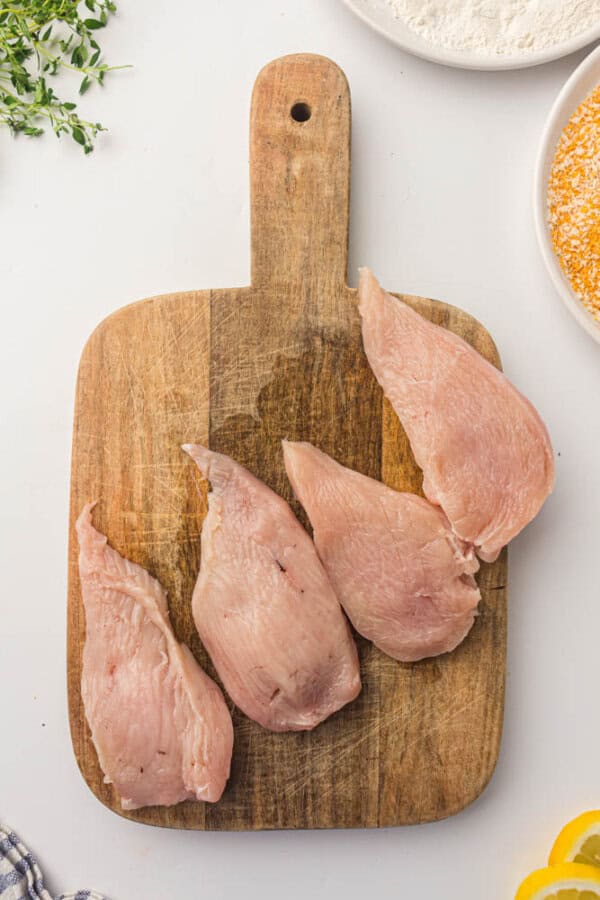 Four chicken breasts on a wooden cutting board on a white table.
