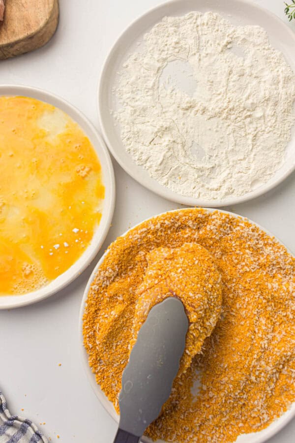 Chicken breast being held by tongs and dipped in panko breadcrumbs.