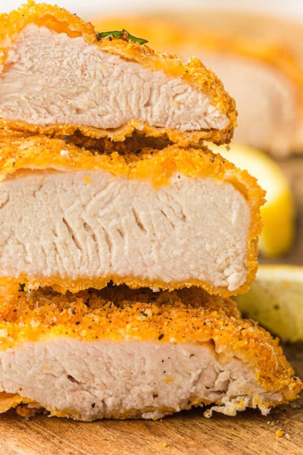 Breaded chicken strips stacked on a wooden cutting board.