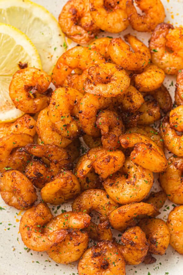 A plate of seasoned and cooked shrimp, garnished with lemon slices and herbs. The shrimp are golden and appear flavorful, showcasing a savory dish.