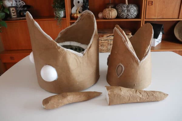 A white tabletop displaying two masks with large mouths covered in decoupaged craft paper.