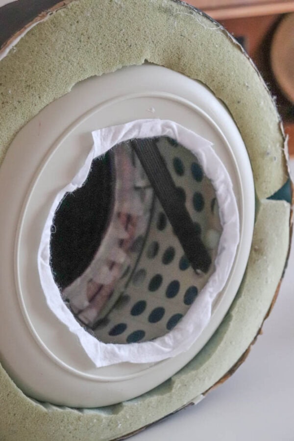 A close-up view of the interior of a large acoustic drum. The drumhead and circular structure are visible, with a white ring outlining the opening. The inner surface appears padded with a green foam lining.