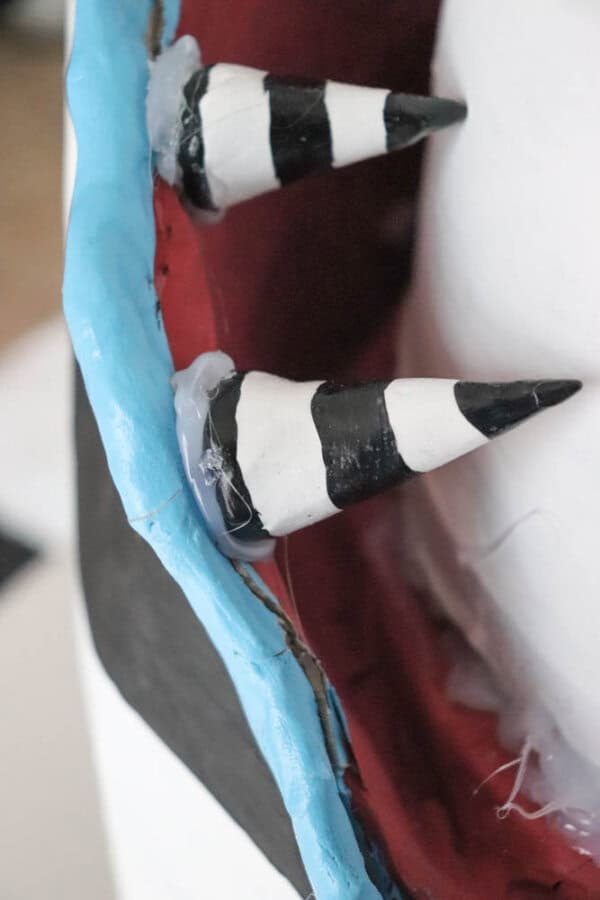 Close-up of two black and white striped cone-shaped objects, resembling teeth, set against a background with blue edging and red interior. The texture appears glossy, with visible adhesive.