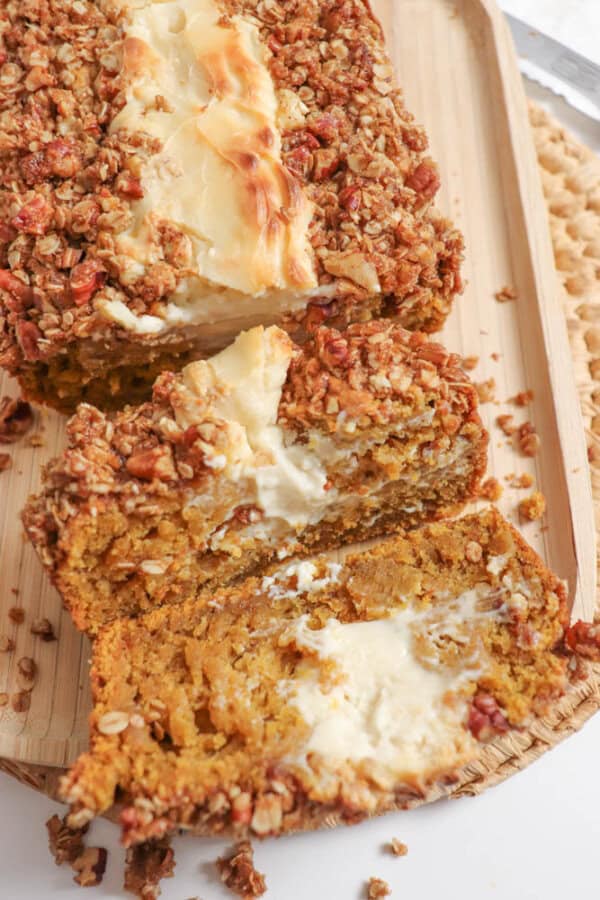 Pumpkin bread, filled with cream cheese with a streusel topping, cut into slices on a wooden board.