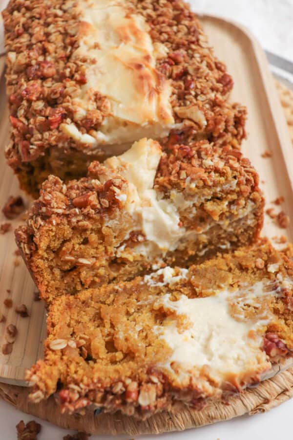 Pumpkin bread, filled with cream cheese with a streusel topping, cut into slices on a wooden board.