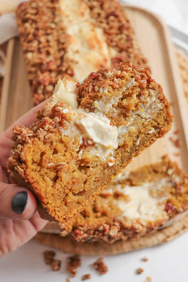 Pumpkin bread, filled with cream cheese with a streusel topping, held in a hand.