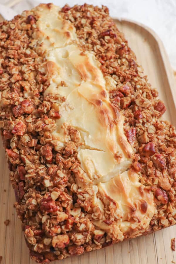 Pumpkin bread, filled with cream cheese with a streusel topping on a wooden cutting board.