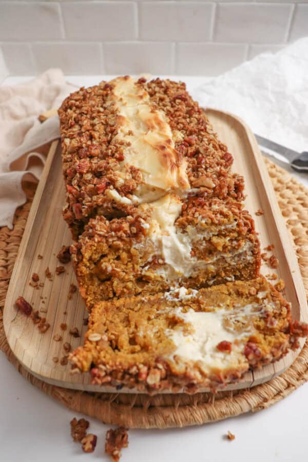 Pumpkin bread, filled with cream cheese with a streusel topping, cut into slices on a wooden board.