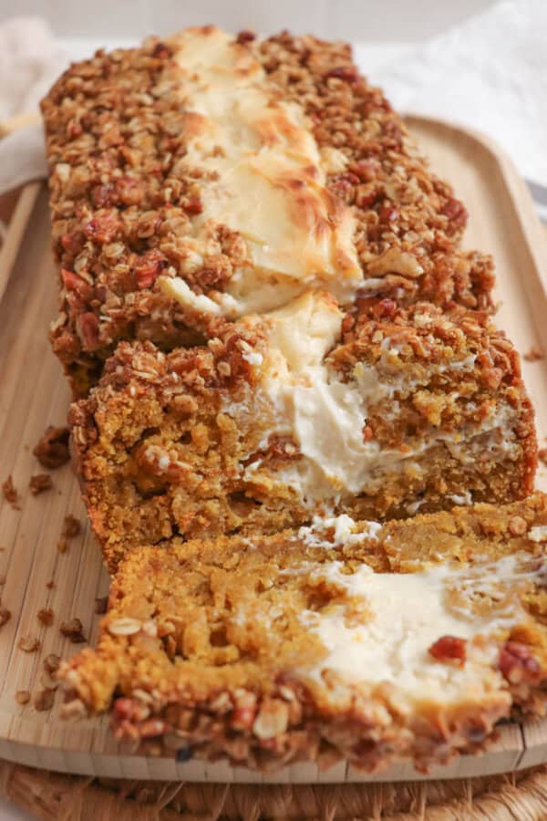 Pumpkin bread, filled with cream cheese with a streusel topping, cut into slices on a wooden board.