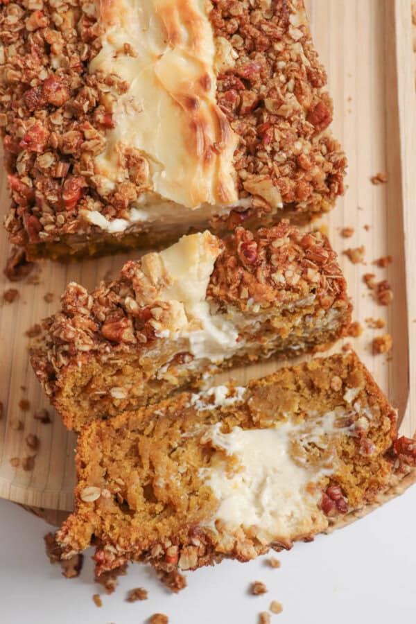 Pumpkin bread, filled with cream cheese with a streusel topping, cut into slices on a wooden board.