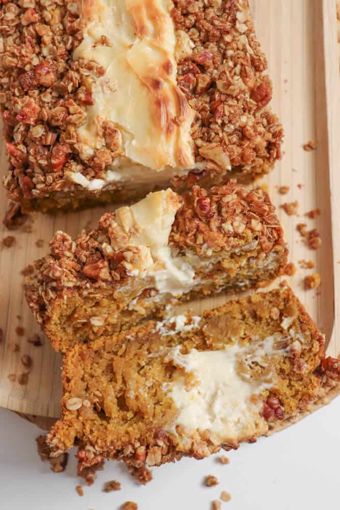 Pumpkin bread, filled with cream cheese with a strussel topping, cut into slices on a wooden board.