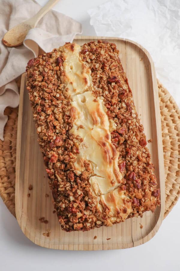 Pumpkin loaf with a cheesecake center and streusel topping on a wooden cutting board.