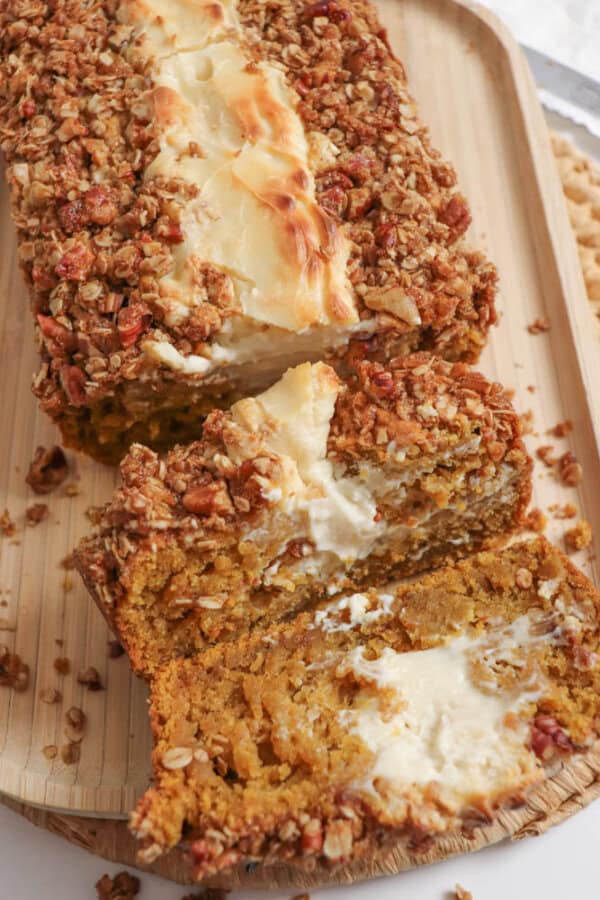 Pumpkin bread, filled with cream cheese with a streusel topping, cut into slices on a wooden board.