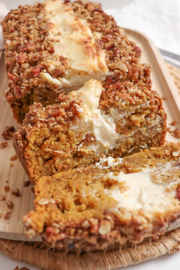 Pumpkin bread, filled with cream cheese with a streusel topping, cut into slices on a wooden board.