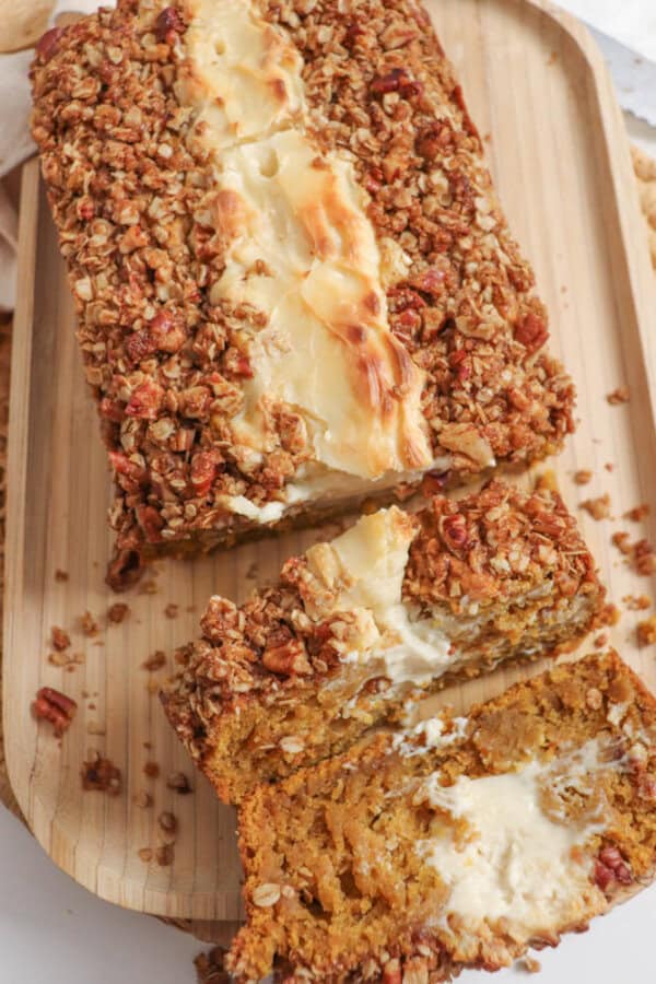 Pumpkin bread, filled with cream cheese with a streusel topping, cut into slices on a wooden board.