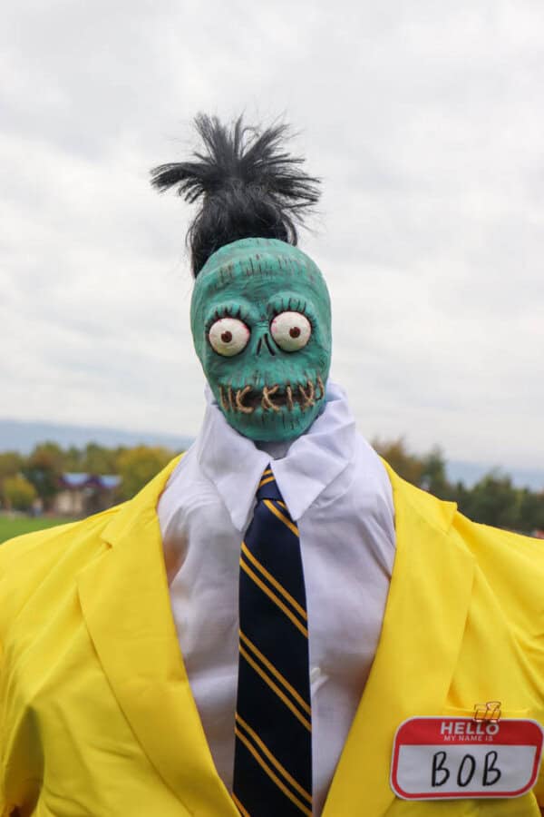 plague doctor costume Zombie shrunken head that looks like Bob from Beetlejuice with a white dress shirt and yellow suit.