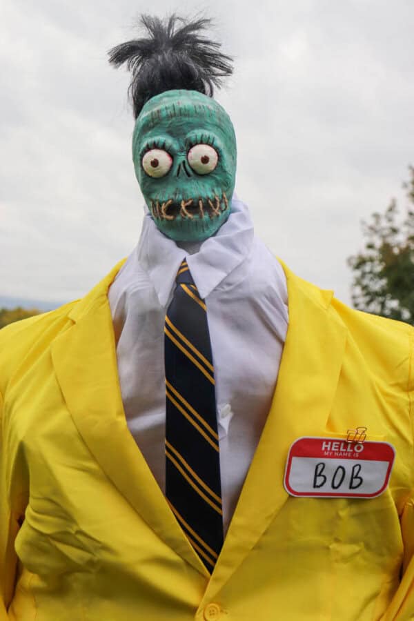 Zombie shrunken head that looks like Bob from Beetlejuice with a white dress shirt and yellow suit.