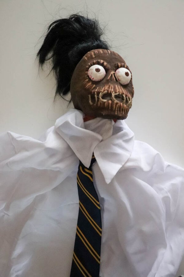 plague doctor costume Zombie shrunken head that looks like Bob from Beetlejuice with a white dress shirt on a white table.