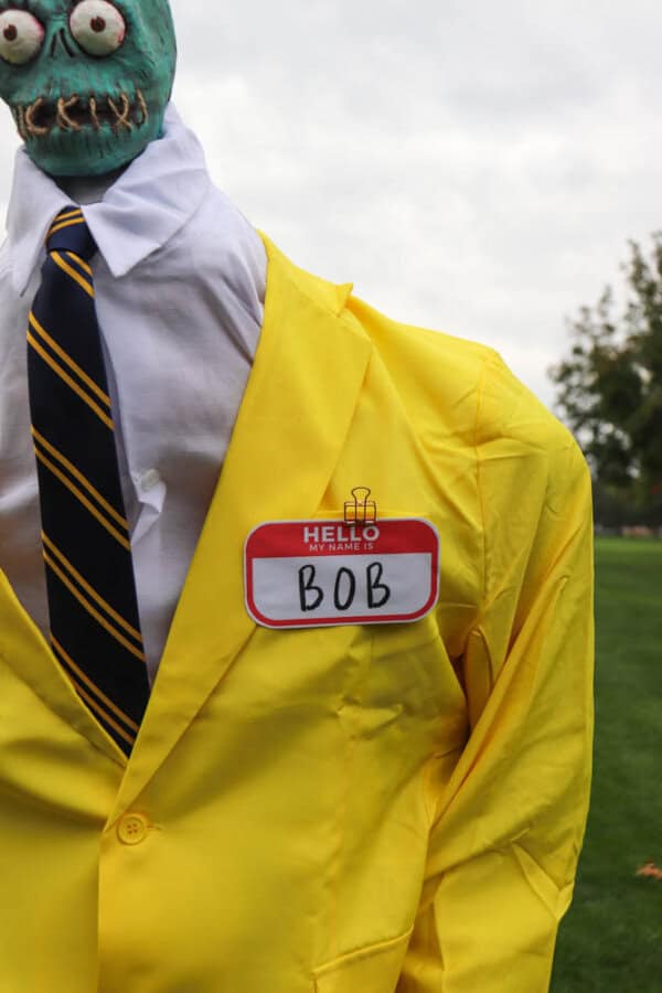 plague doctor costume Zombie shrunken head that looks like Bob from Beetlejuice with a white dress shirt and yellow suit.