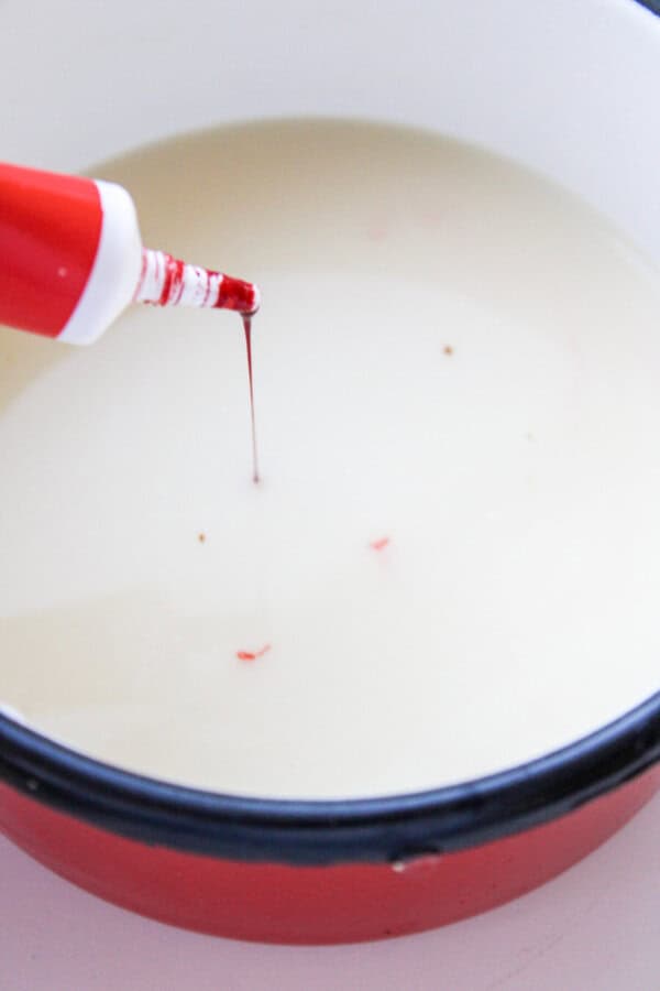 Red food colouring dripping into a red saucepan with milk in it.